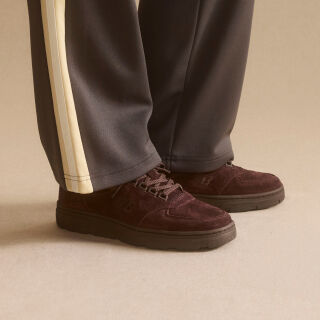 Knee down view of a man wearing a pair of New Balance Made in UK sneakers standing on a patterned tile floor.  