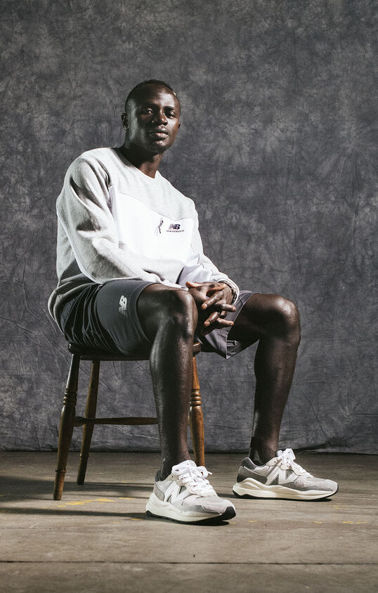 Sadio Mané sitting on chair in studio wearing grey NB apparel and shoes.