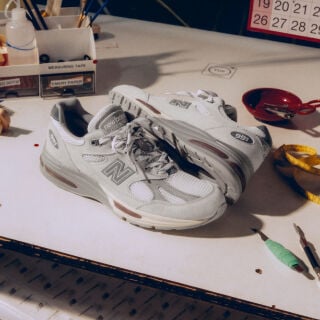A pair of New Balance Made in UK sneakers on a white workbench surrounded by shoemaking tools and other textile equipment. 