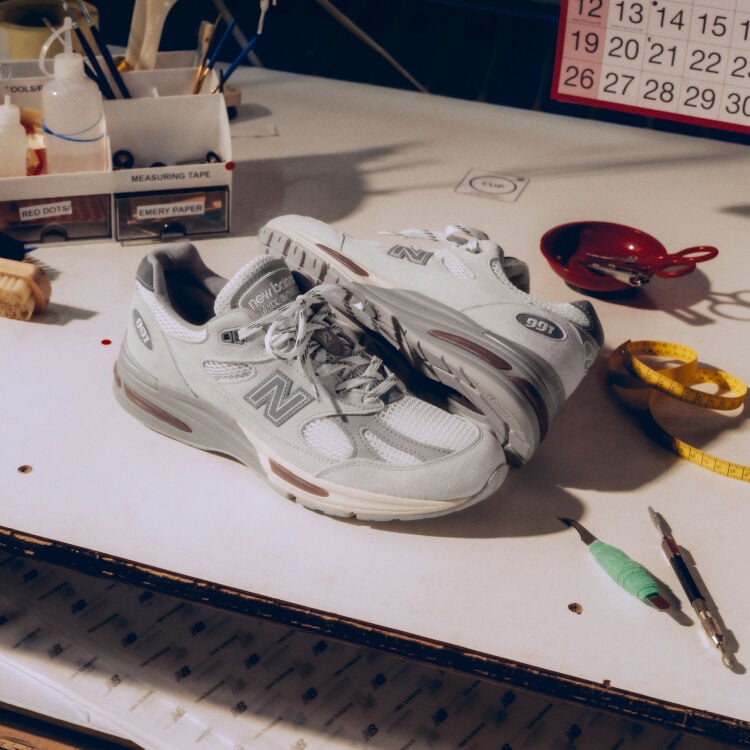 A pair of New Balance Made in UK sneakers on a white workbench surrounded by shoemaking tools and other textile equipment. 